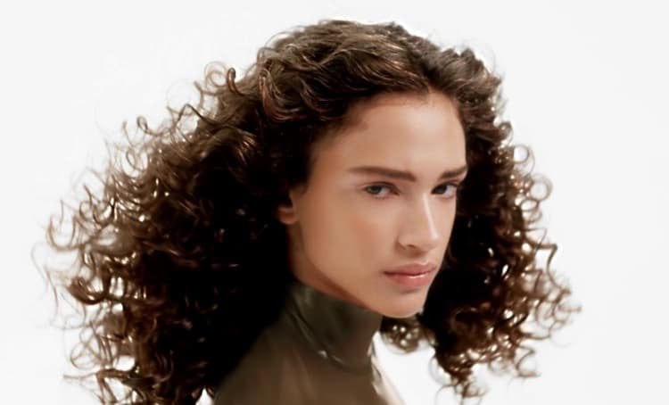 Mulher posando e exibindo seus cabelos cacheados saudáveis, radiantes e bem definidos, com movimento, definição e brilho natural.
